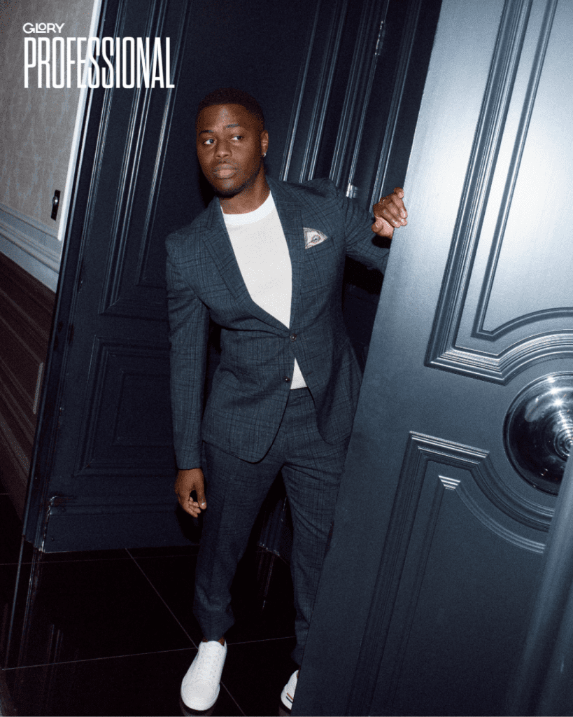 Man wearing green suit with white t-shirt and sneakers peaking out from a set of big blue doors.