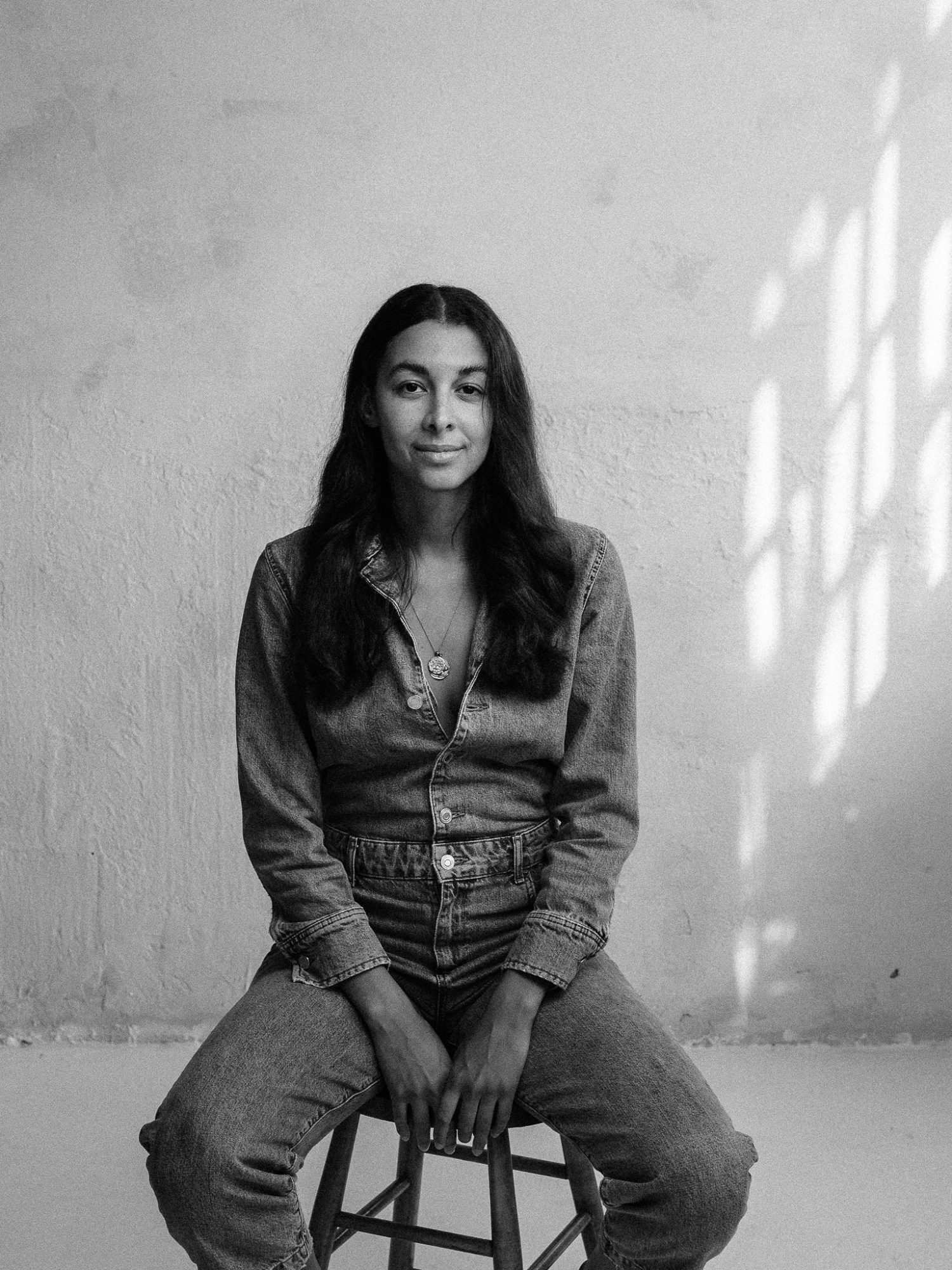 Black and white image of Daphné Eastmond in a denim shirt and jeans sitting on a stool and looking into the camera.