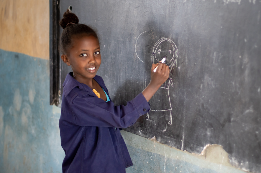 Child in purple shirt drawing on chalkboard