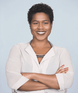Woman in a white blouse with dark red lipstick on, smiling at the camera.