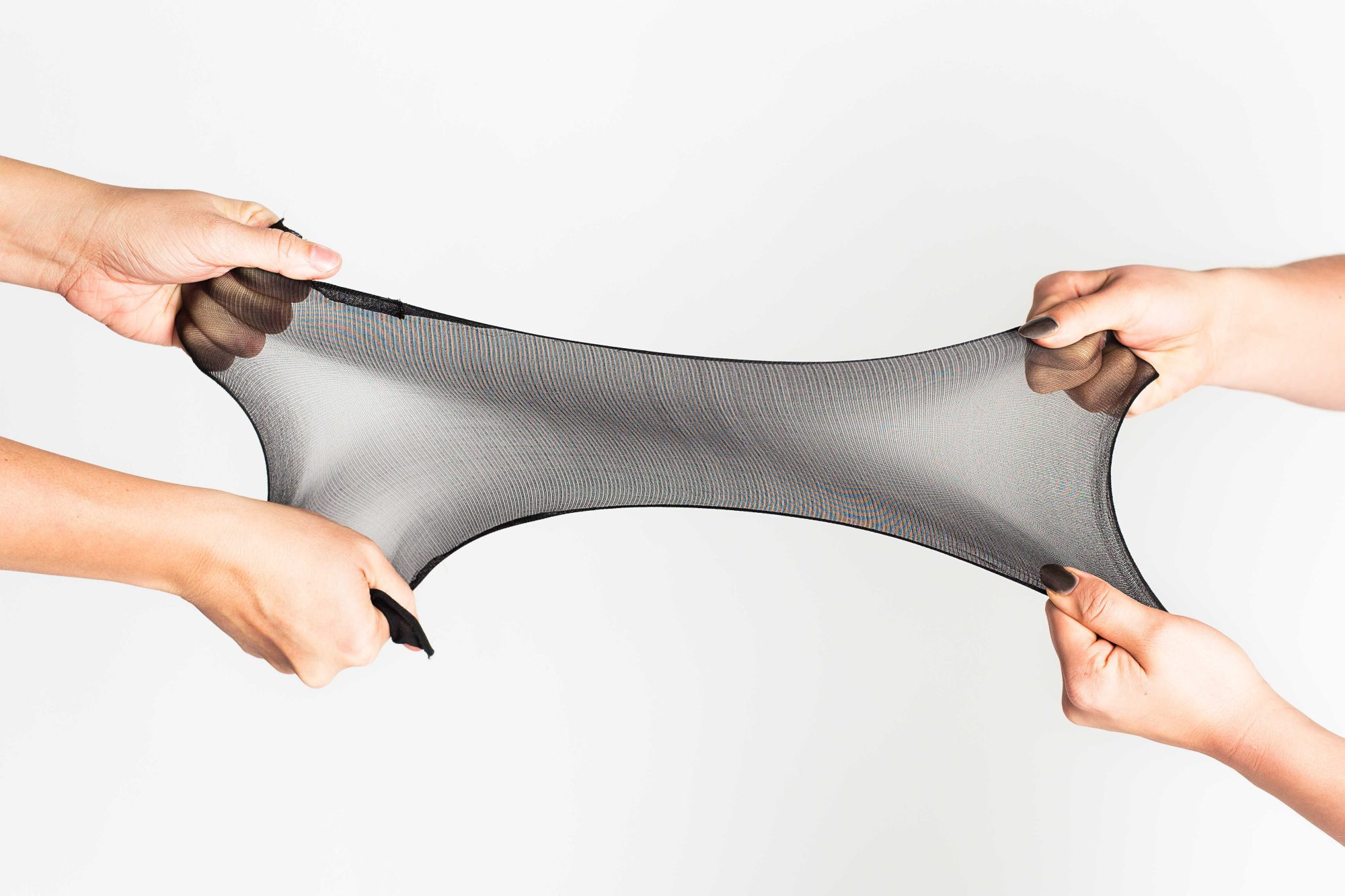 Two pairs of hands stretching a pair of black Sheertex stockings.