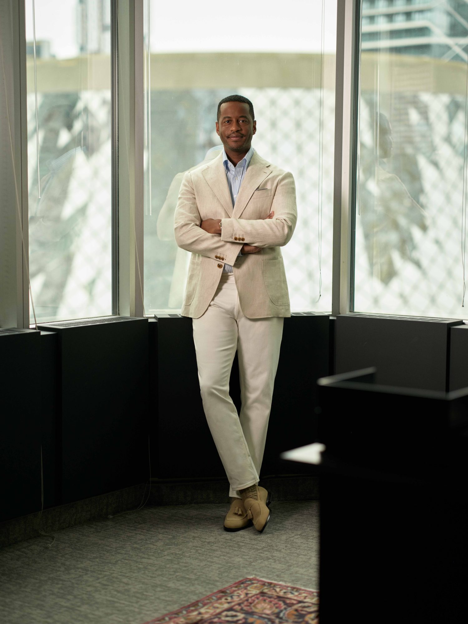 Toronto Symphony Orchestra CEO Mark Williams standing in a white suit with arms crossed and leaning against a wall in his office.