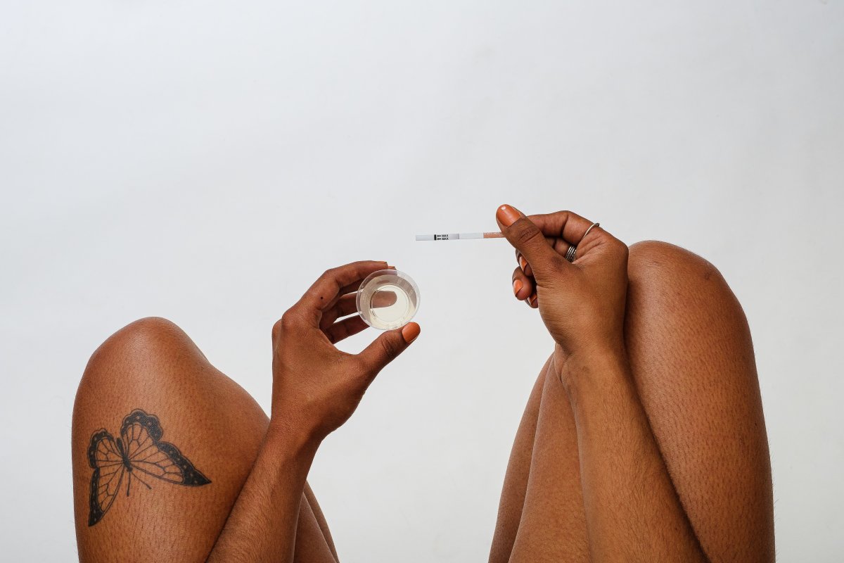 An unseen woman holds a cup of urine in one hand and an OVRY pregnancy test in the other