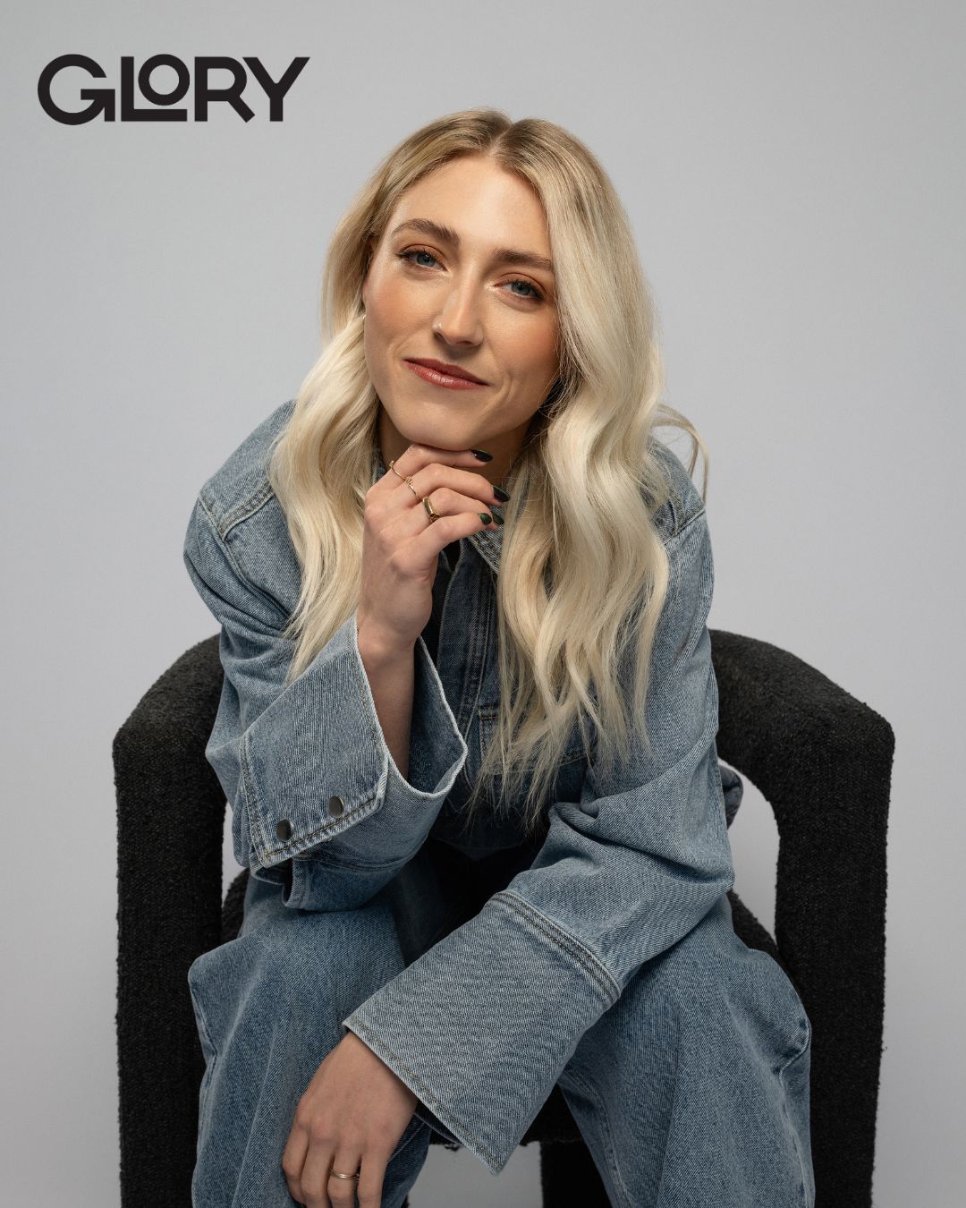 Piper Gilles sitting in a chair wearing a denim jacket and jeans.