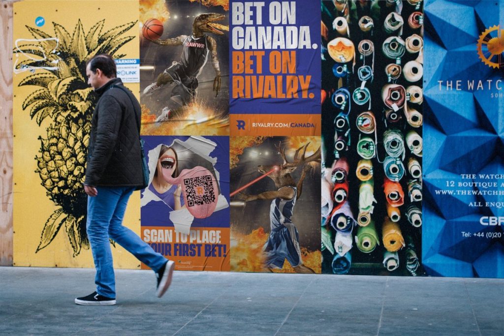 Man walks in front of Rivalry sports betting advertisements