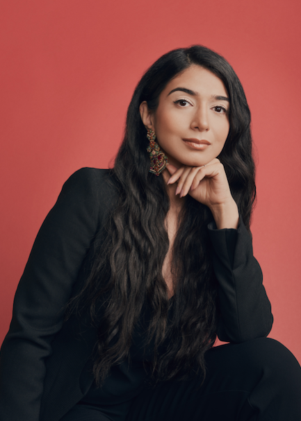 Our Place founder Shiza Sheed sitting with hand under chin looking thoughtful wearing black against red background