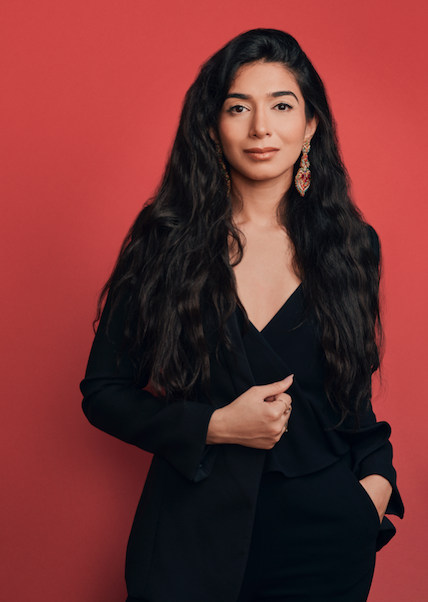 Our Place founder Shiza Shahid wearing black and standing against a red wall