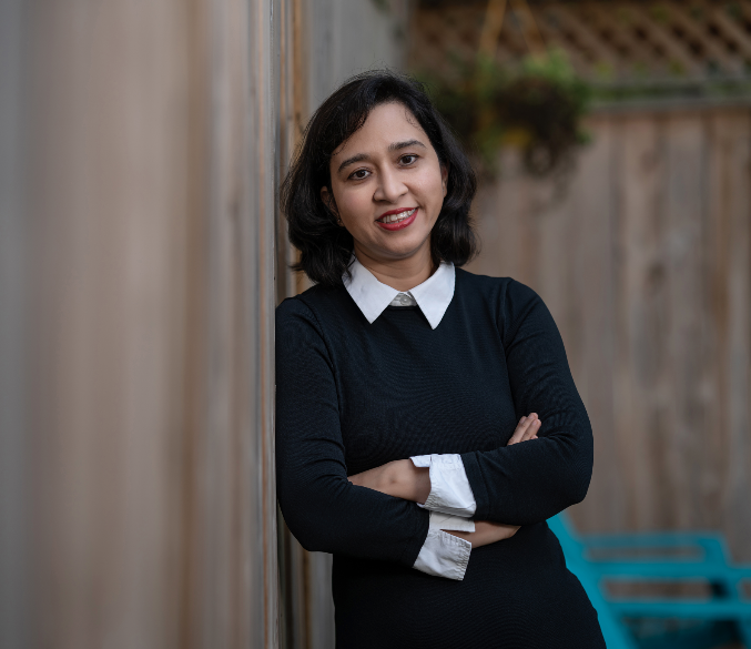 Khushboo Jha in sweater leaning against fence